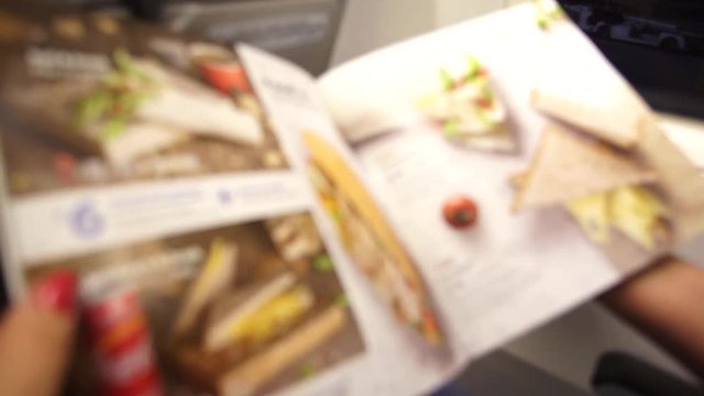 Blurry video of female passenger turning paper pages of catering menu while sitting on her place on board of plane. Woman ordering food during flight. Real time 4k video footage.