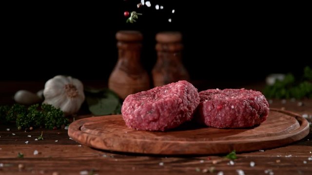 Super slowmotion footage of strewing salt and herbs at fresh raw beef meat burger, 1000fps, 4K