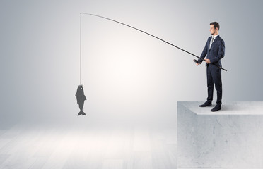 Young businessman fishing golden fish from the top of a building
