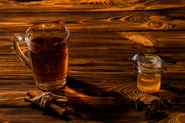 Black aromatic tea in a glass transparent cup. Glass jar with gold honey on a rustic brown wooden table. Copy space.