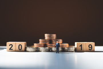 Miniature people, businessman standing with stack coins and year 2019 using as business and financial concept