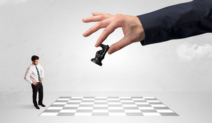 Little businessman thinking about chess strategy with a big hand concept
