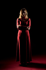 Fototapeta premium Lady in red gown standing and posing in studio. Portrait of beautiful elegant woman in evening dress