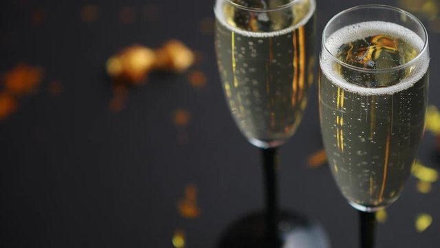 Two glasses full of sparkling champagne wine with golden decoration of confetti and serpentines on black elegant background. Top view with copy space. Festive or party concept.