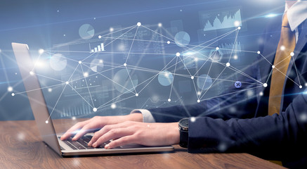 Businessman typing on laptop with linked reports charts grapghs around
