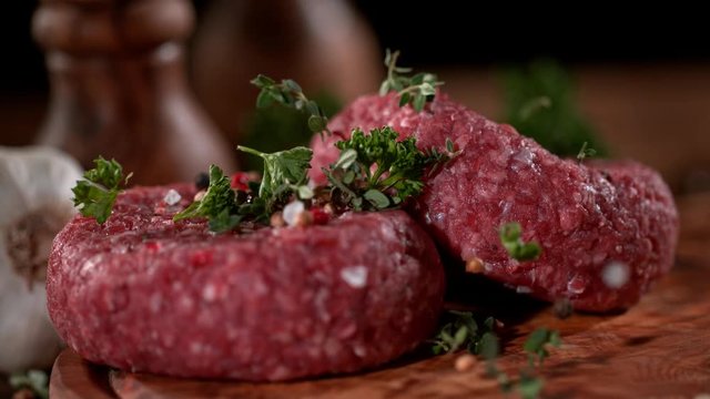Super slowmotion footage of strewing salt and herbs at fresh raw beef meat burger, 1000fps, 4K