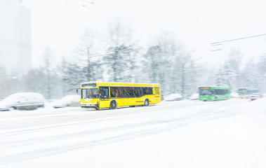 Yellow city bus rides a snowbound road during a snow storm. Abstract blur background. Concept of...