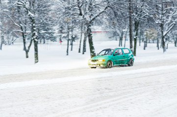 Driving in snow. Motion in blur small green car in heavy snowfall in city road. Abstract blur winter weather background