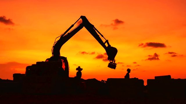 Construction Video At construction site The silhouette excavator is digging ground and lifting a large mortar, with engineering and construction workers to help with colorful sunset .