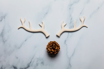 Christmas reindeer face made from antlers and pine cone on a marble background