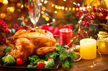 Christmas family dinner. Roasted chicken on holiday table, decorated with gift boxes, burning candles and garlands. Roasted turkey over wooden background