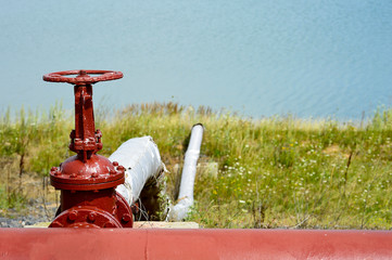 The valve from the pipeline against the background of the factory and an artificial lake