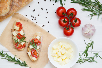 Italian bruschetta toasts with tomatoes and cheese on white wooden background, top view