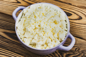 Full violet ceramic bowl of fresh homemade curd on old brown wooden table
