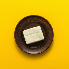 Plate with piece of butter on yellow background, top view, flat lay