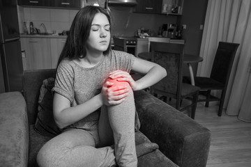 young woman has knee pain, black and white photo red accent