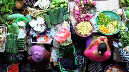 Urban scene of female street market trader selling fresh flowers and spices to Indonesian tourists and local people 