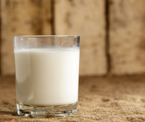 A glass of milk stands on a burlap on the background of old boards.