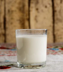 A glass of milk stands on a burlap on the background of old boards.