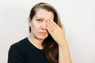 A sad woman on a light background closed one eye with her hand because she had a conjunctivitis. The woman has red eyes, they are red and hurt