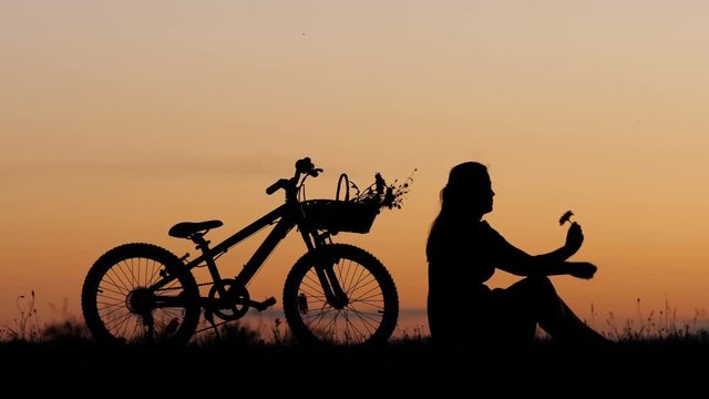 Single woman silhouette sit on hill and smell a flower, romantic bike ride 