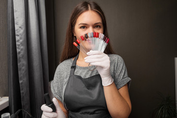 happy  young woman profession manicurist with polish and nail color palette on gray background