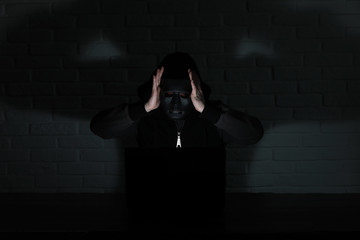 Hacker in black mask and hood at the table