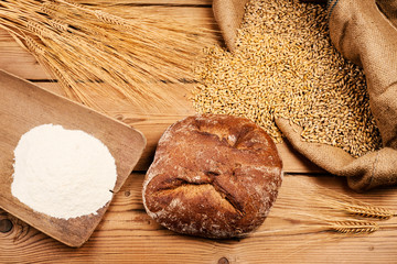 Brot mit Mehl, Getreide und Ähren auf Holztisch