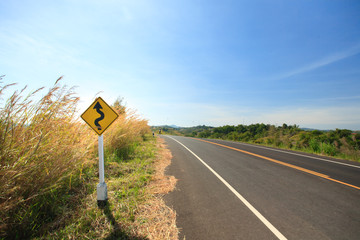 Traffic signs erected at the side of road with grass flower , clearly blue sky  in countryside of Thailand.