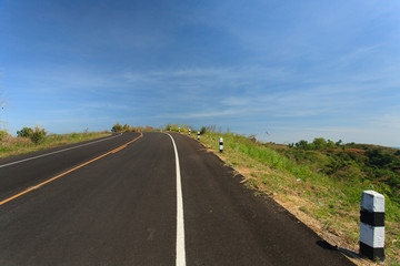 Road with grass flower , clearly blue sky  in countryside of Thailand.