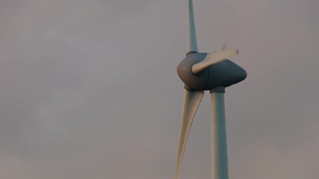 Wind turbine with turning blades in the wind in an offshore windpark during sunset.