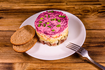 White plate with russian traditional new year salad herring under fur coat and rye bread on wooden table