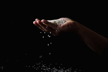 Fototapeta na wymiar Rice falling through the fingers of male hand. Dark background