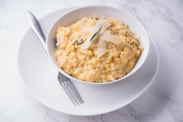 Pumpkin risotto with parmesan and sage. White marble background