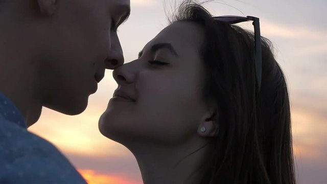 Cutie girl kissing her happy boyfriend touching his nose at sunset in slow motion  