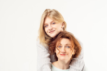 Young blonde teenage girl embracing beautiful red haired woman standing on white background. Lifestyle and family