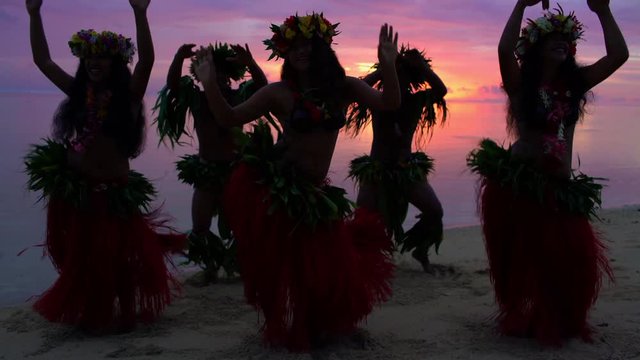 Group of beautiful young synchronized Polynesian males and female dancers at sunset on the beach entertaining in traditional costumes barefoot South Pacific