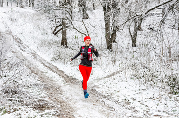 Young woman athlete in red leggings runs in the winter forest. Direct view. Winter sports. Extreme running.