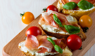 Italian tomato, prosciutto, jamon, ham and cheese bruschetta. Tapas, antipasti with chopped vegetables, herbs and oil on grilled ciabatta and baguette bread.