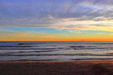 Sunrise on the beach. A sailing yacht in the open waters of the Mediterranean Sea. Maritime landscape with the vivid colors of daybreak at Malvarrosa Beach, Valencia, Spain.