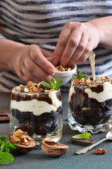 Light low-calorie dessert with cream, nuts and fruits on a concrete background. Female hands. Selective focus.