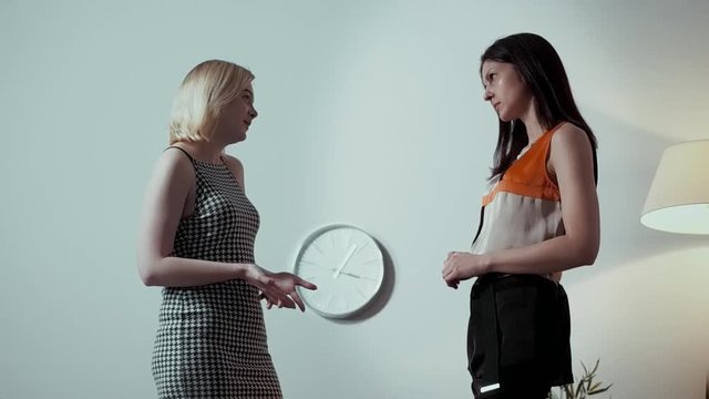 Two lesbians are talking in a bright spacious room, two cute friends are discussing their boyfriends, blonde and brunette are sitting on the armchairs, a room in a minimalist style