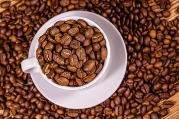 White cup filled with coffee beans on wooden table. Top view