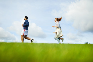Side view of active guy and girl running in the morning on background of cloudy sky