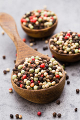 Peppercorn mix in a wooden bowl on grey table.