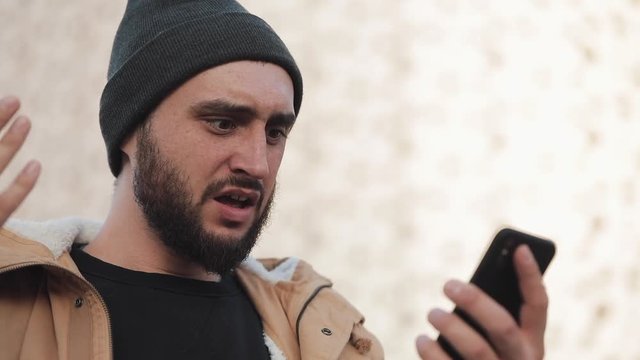 Young man reading bad news on smartphone standing near office center. he looks shockes and worried while checking news on smartphone. Lost businessman. Unsuccessful bet on the sport