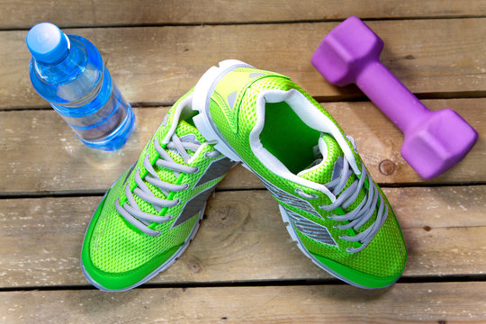 Sports sneakers, dumbbells, drinking water on a wooden background
