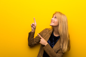 Obraz premium Blonde girl on vibrant yellow background pointing with the index finger and looking up