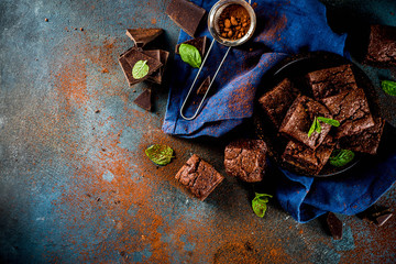 Homemade chocolate brownies with chocolate powder and mint leaves on dark background, top view copy...