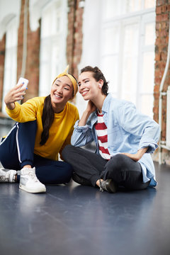 Two young female hip hop dancers sitting on the floor of studio and making selfie
